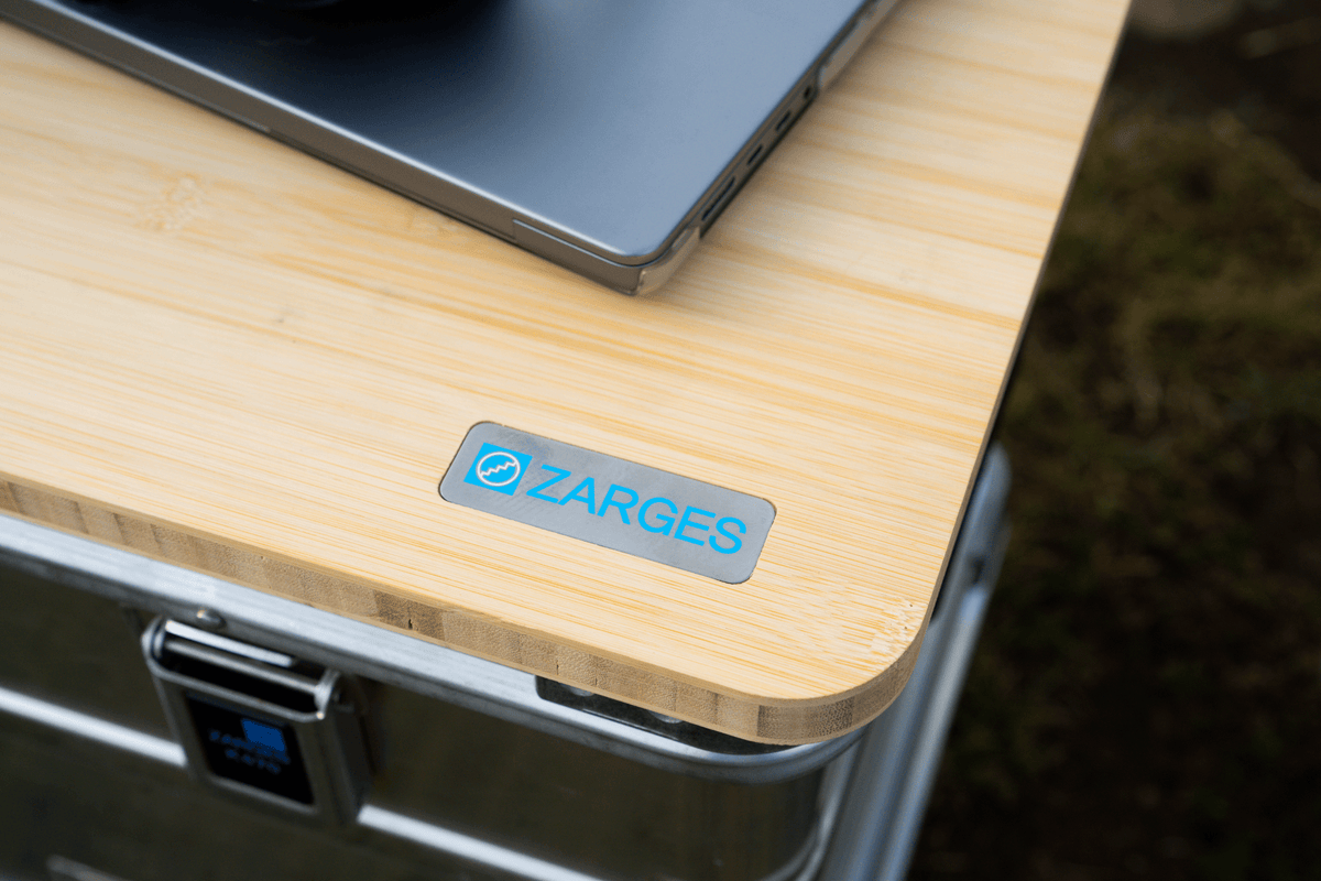 Close-up of the ZARGES Bamboo Travel Top corner and badge with a laptop resting on it, case below