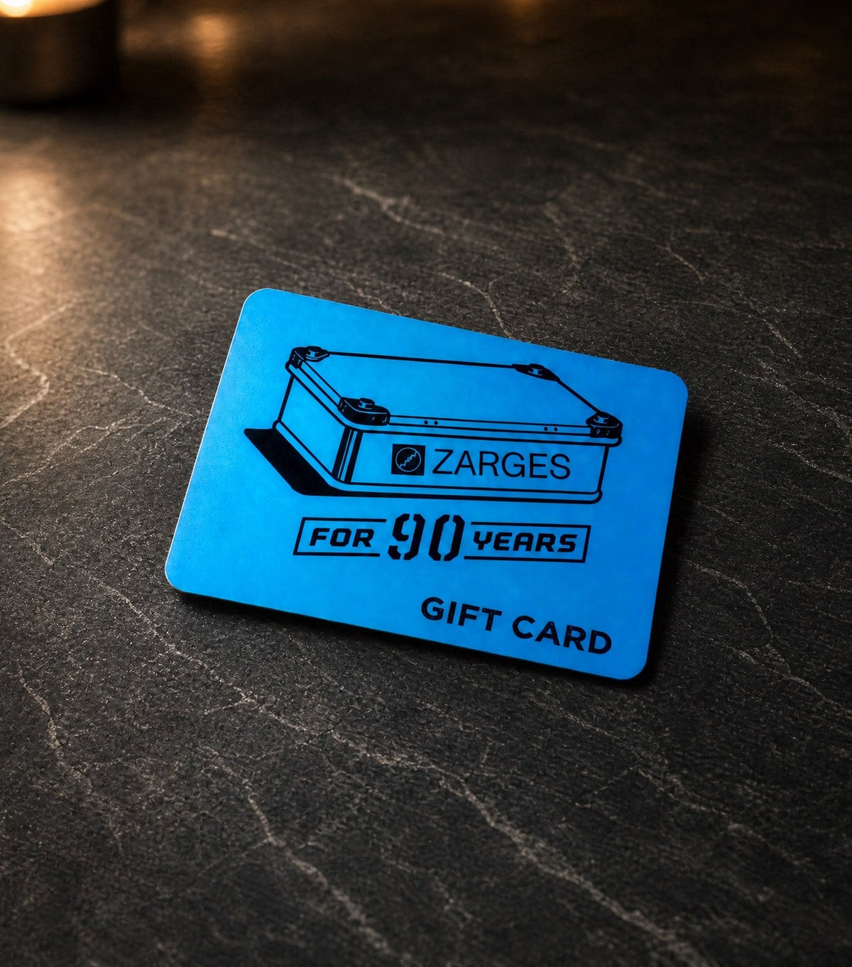 ZARGES Gift Card, 90th anniversary edition, centered on a dark stone surface with candlelight