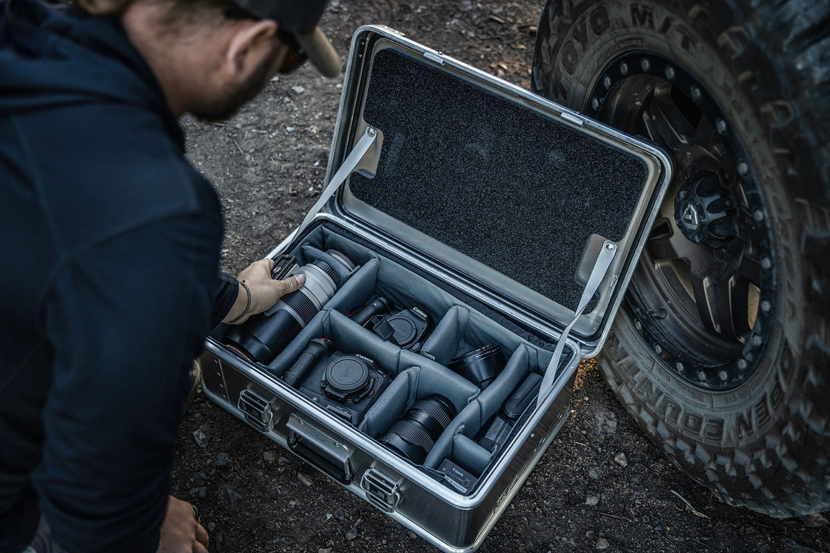 Photographer reaches into an open ZARGES case beside an off-road tire, lenses sorted by the Interior Divider Set