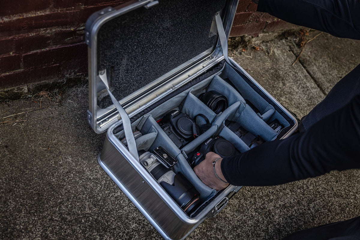 Hand placing gear into an open ZARGES case on pavement by a brick wall, Interior Divider Set compartments