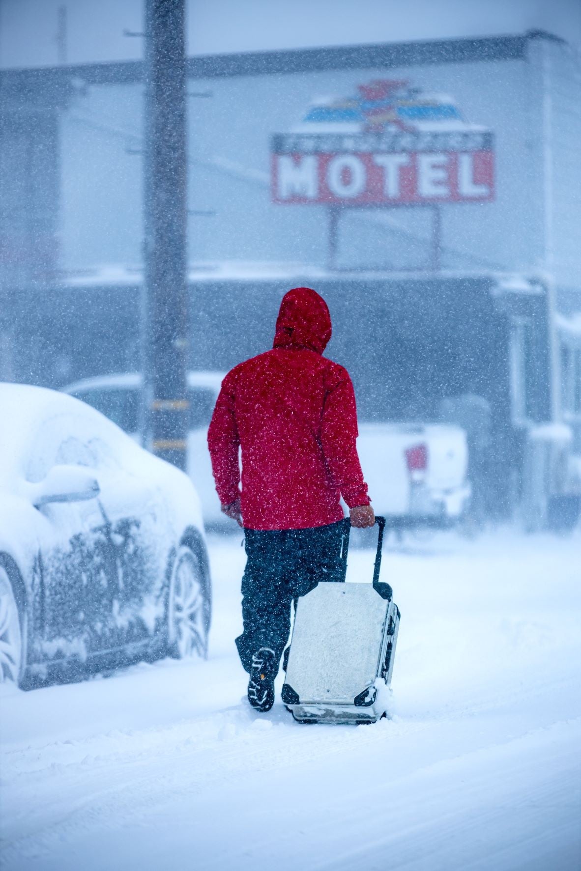 Traveler in a red jacket pulls a ZARGES K424 XC-41810 rolling case down a snowy street toward a motel
