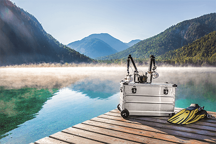ZARGES K424 XC-41812 case on a lakeside dock with underwater camera rigs on top and dive fins
