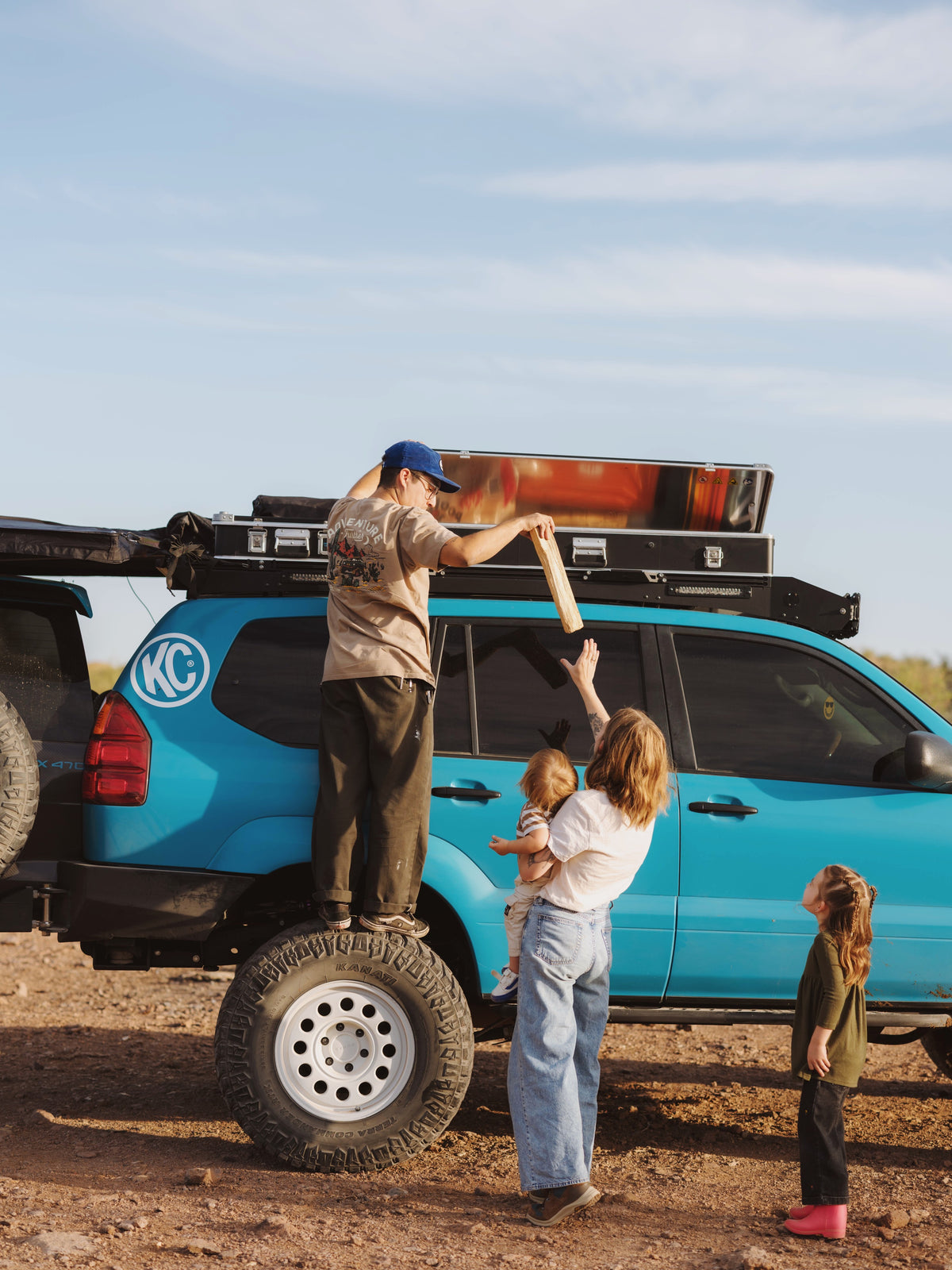 Family unloads a ZARGES K470-31011686 case from a roof rack on a teal SUV in the desert