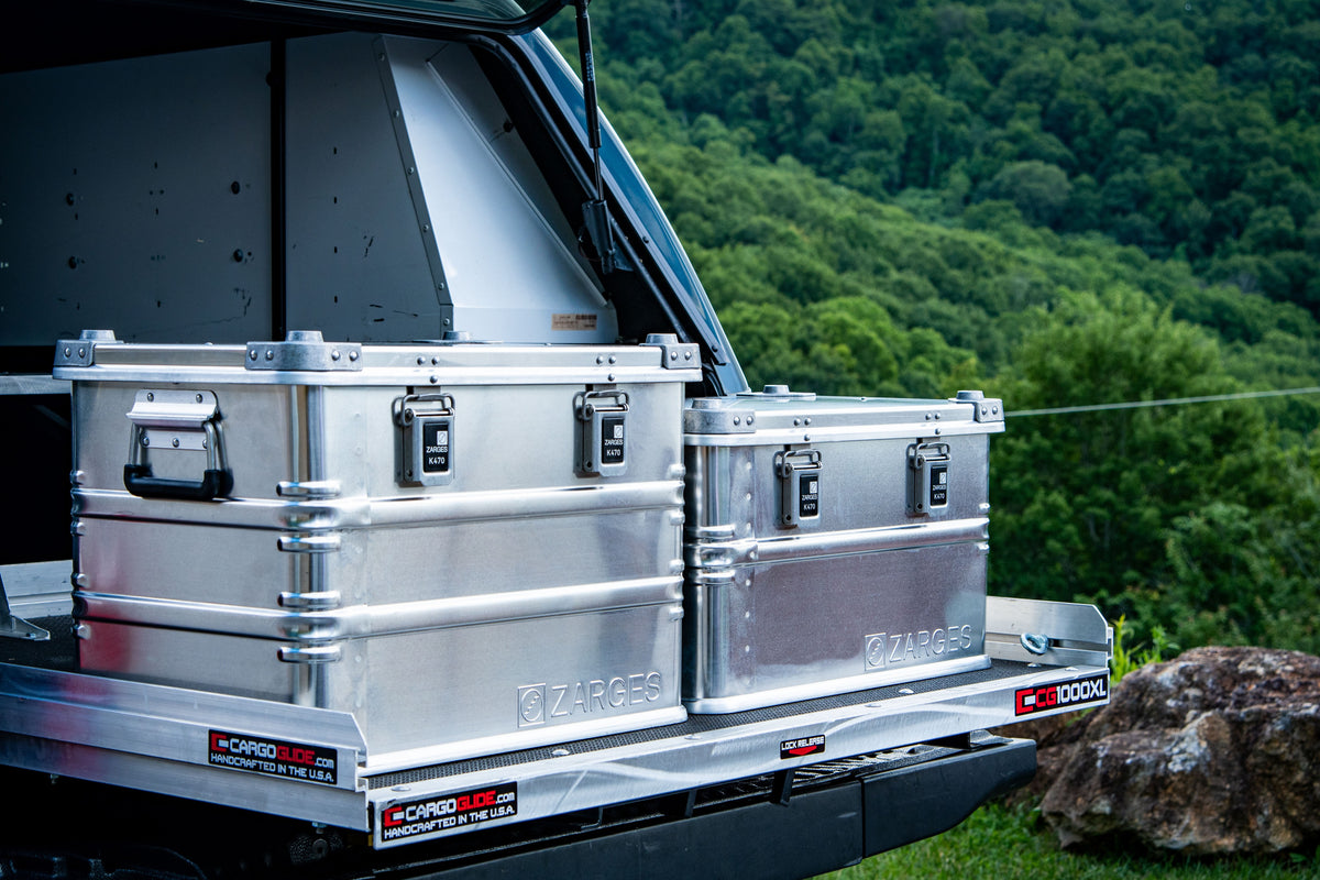 Two ZARGES K470-40564 cases on a truck bed slide-out with a forested hillside behind