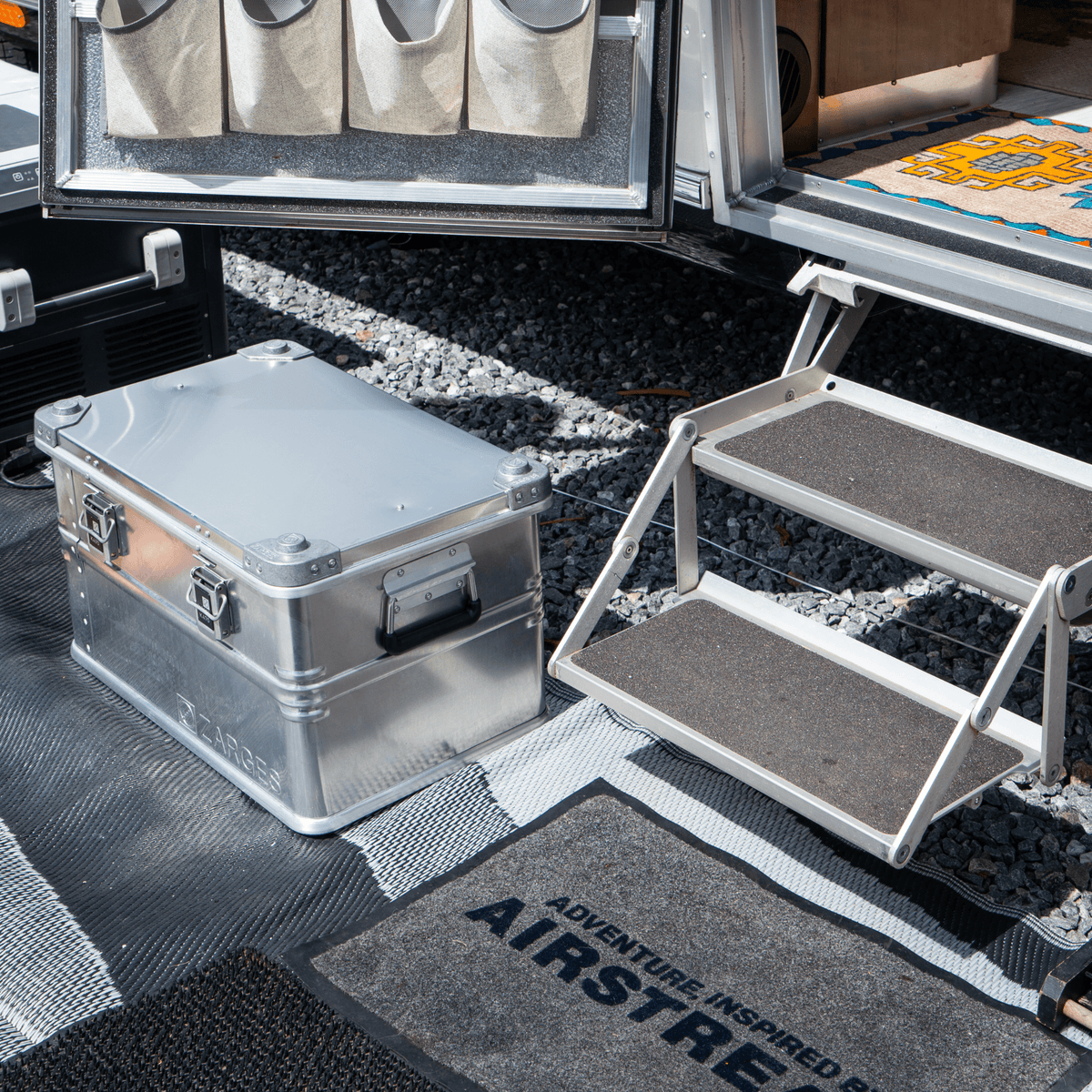 ZARGES K470-40678 case, closed, on an outdoor mat beside an Airstream trailer's entry steps