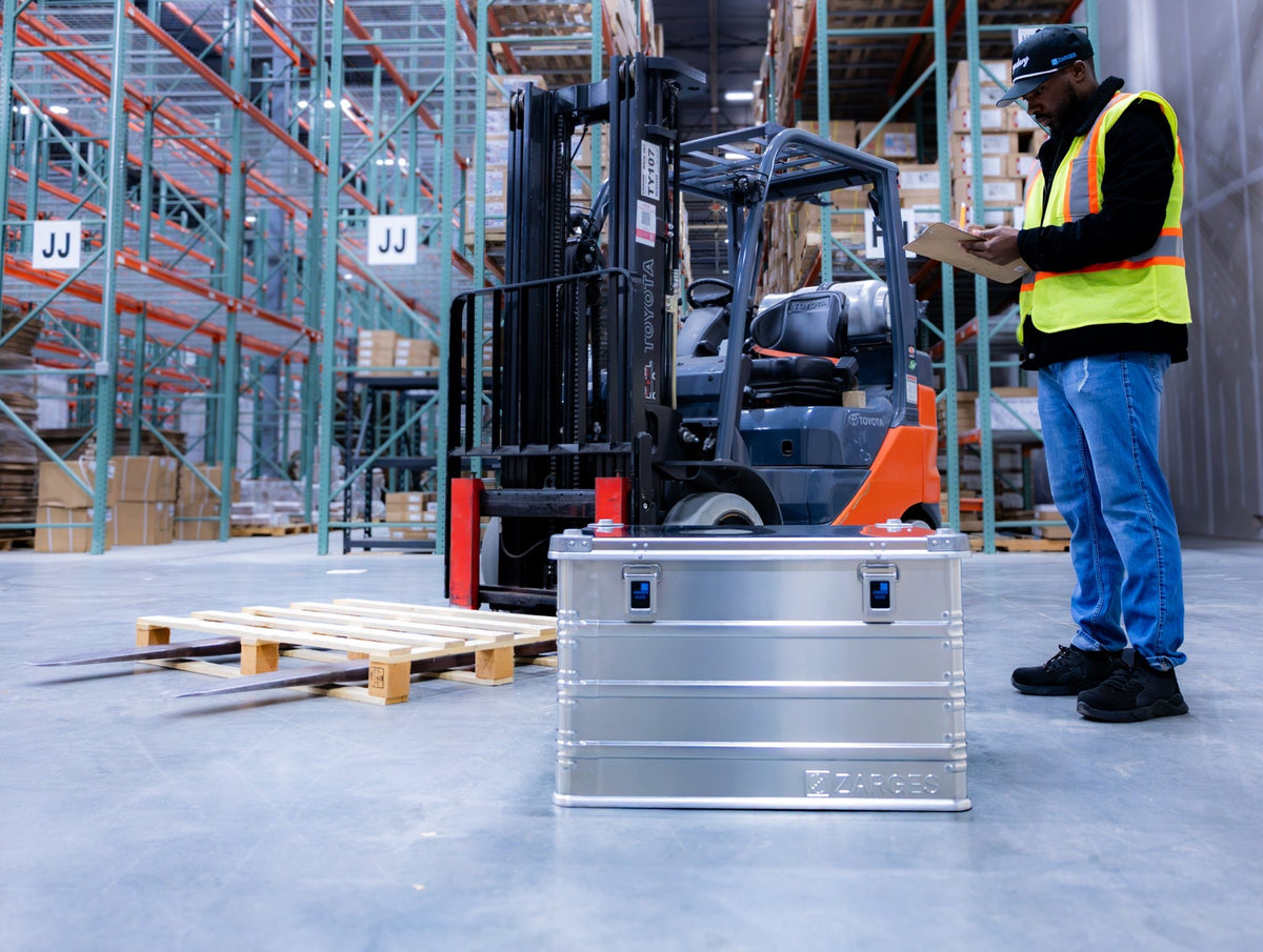 ZARGES K470-40843 aluminum case on a warehouse floor by a forklift as a worker checks a clipboard