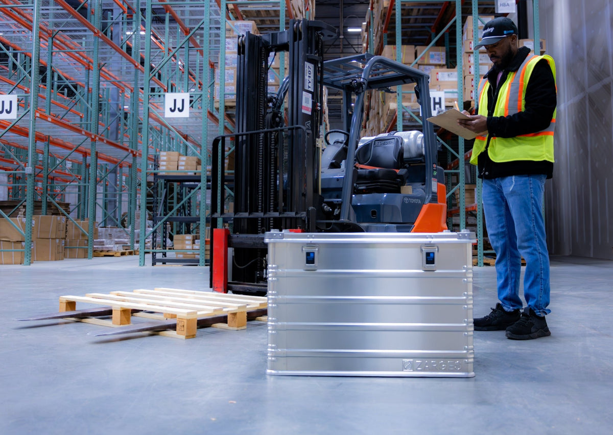 ZARGES K470-40844 case on a warehouse floor beside a worker reading a clipboard near a forklift