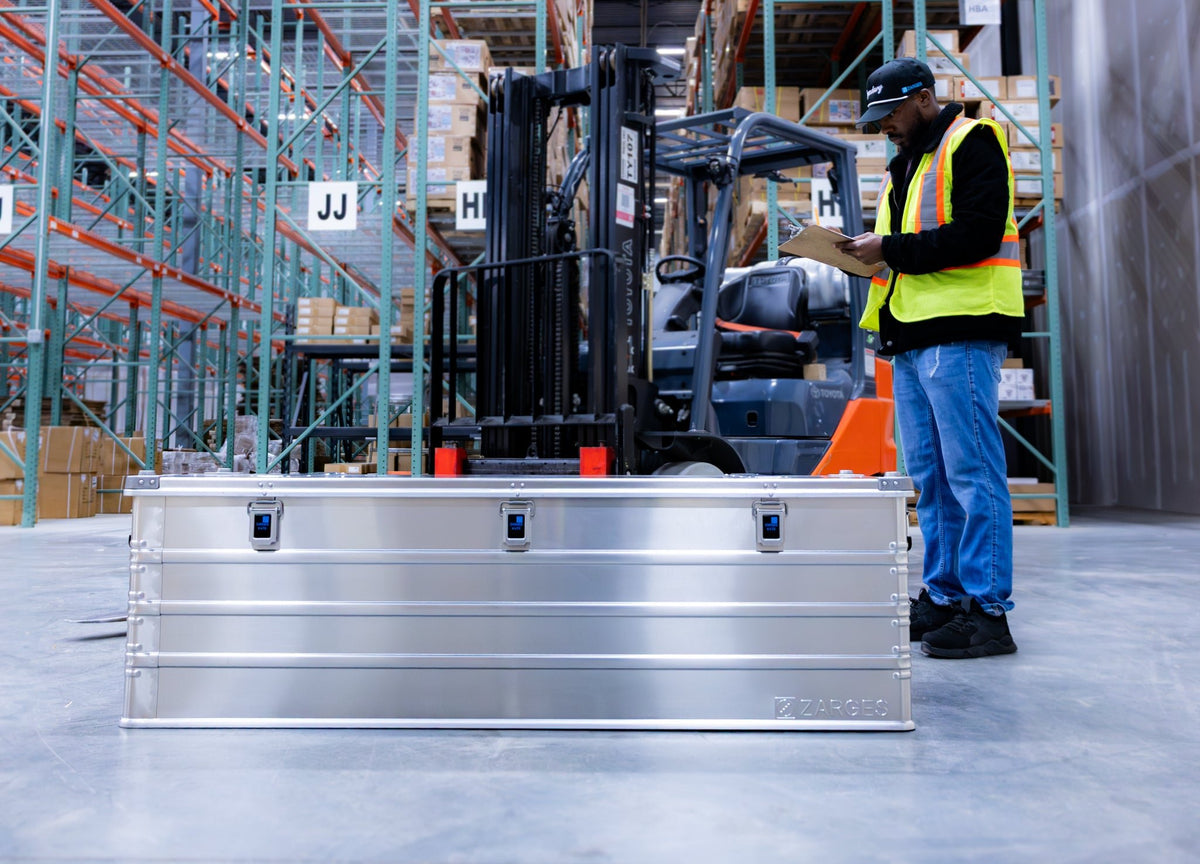 ZARGES K470-40875 long case on a warehouse floor as a worker in a safety vest checks a clipboard by a forklift