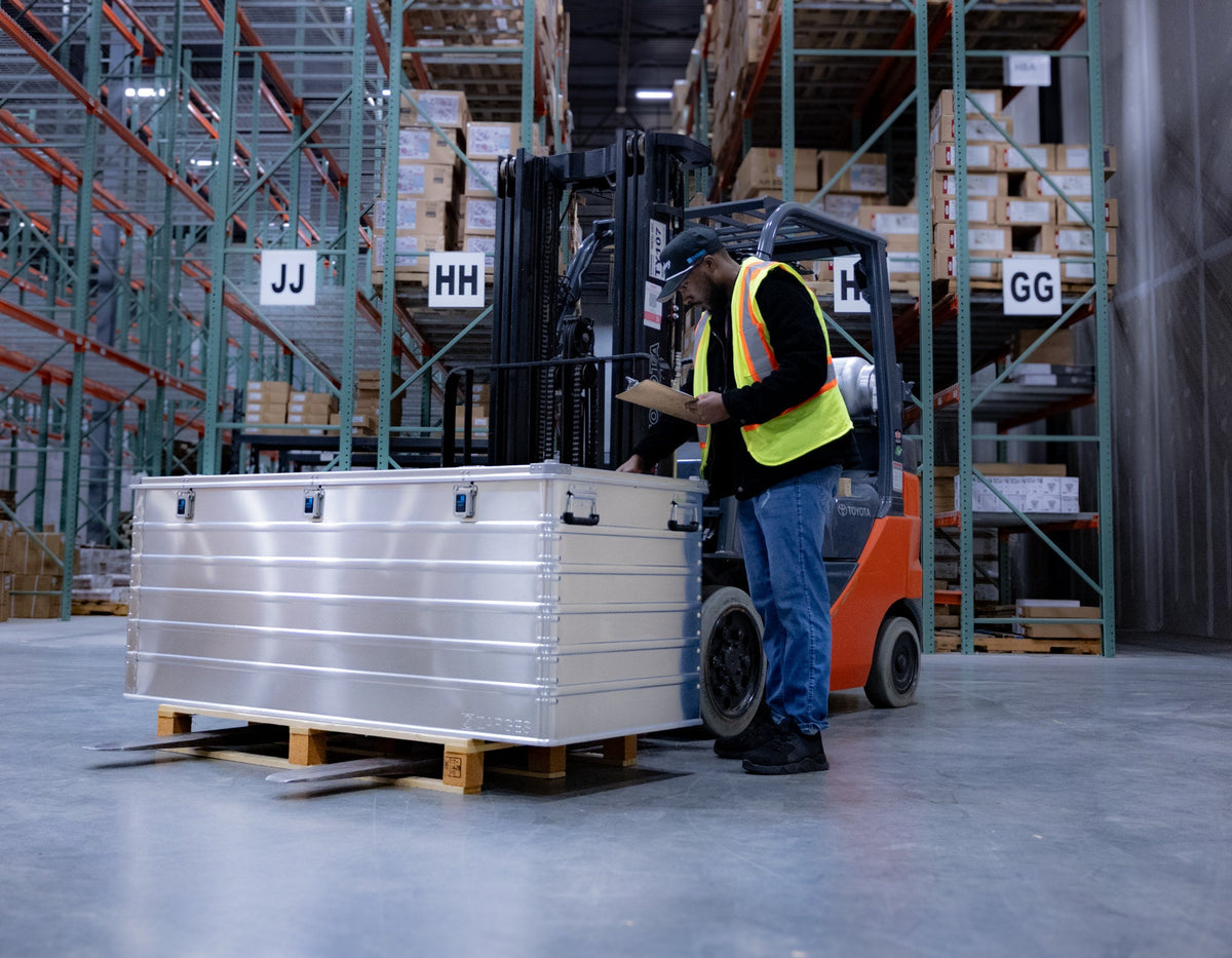 Warehouse worker with a clipboard beside a ZARGES K470-40876 large aluminum case on a pallet