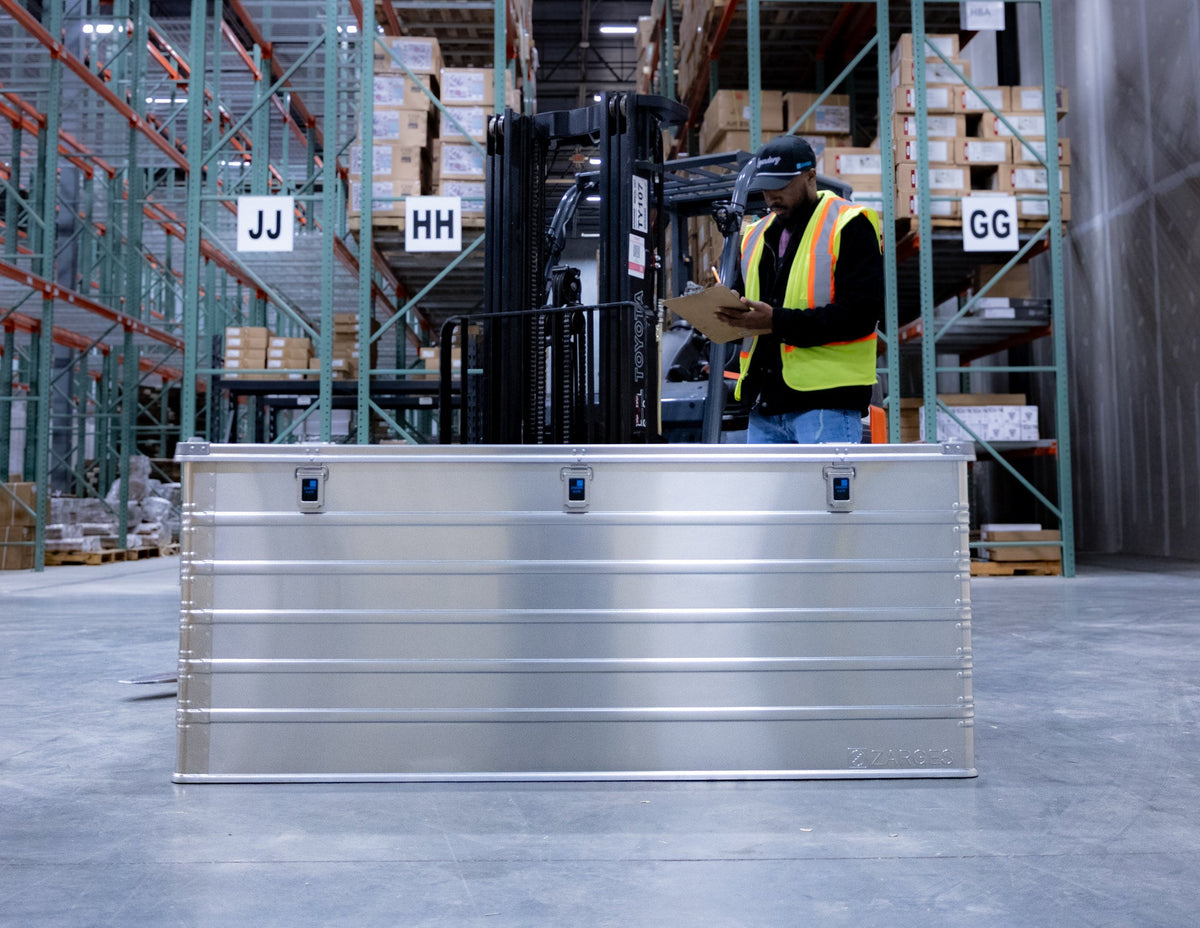 ZARGES K470-40876 large aluminum case on a warehouse floor in front of a worker with a clipboard