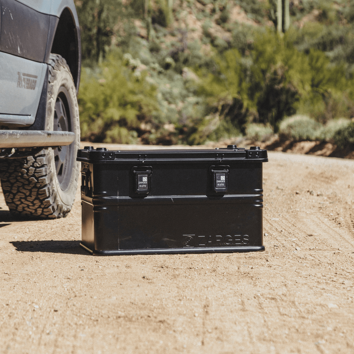 ZARGES K470-Matte Black-31013205 case on a desert dirt road beside an off-road truck's tire