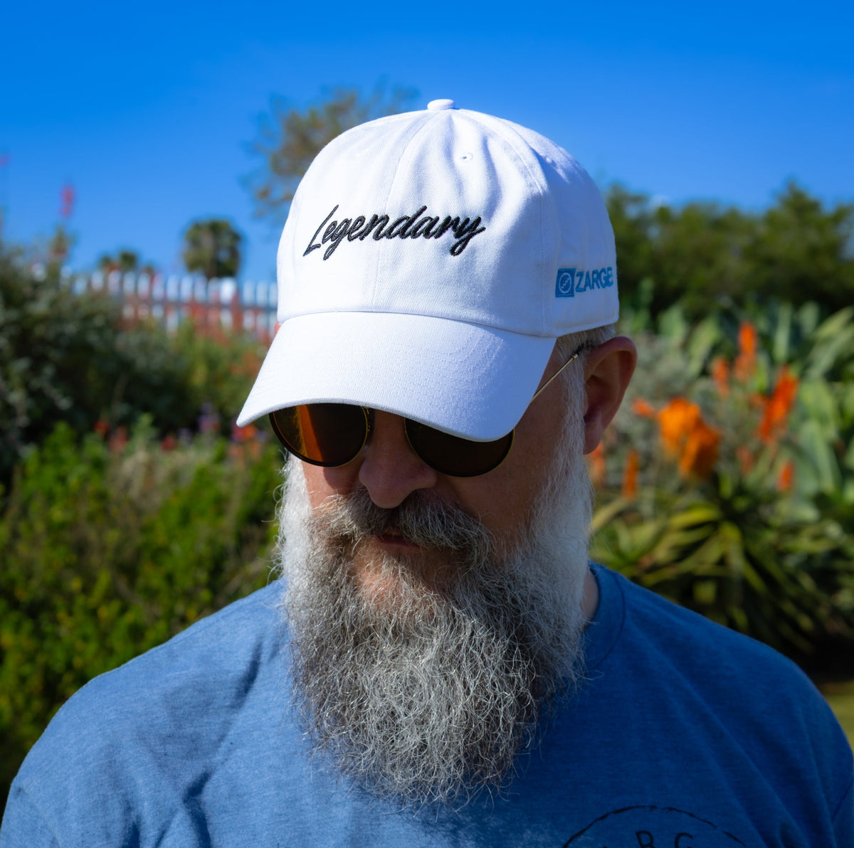 Bearded man in sunglasses wearing the white ZARGES Legendary 47' Hat in a sunny garden