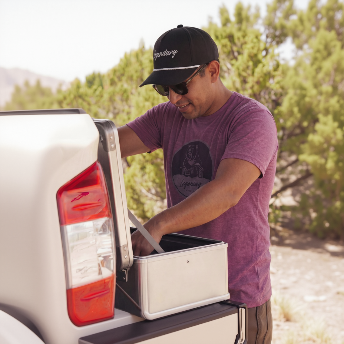 Man in the ZARGES Legendary Bear T-Shirt and cap reaches into an aluminum case on a truck tailgate