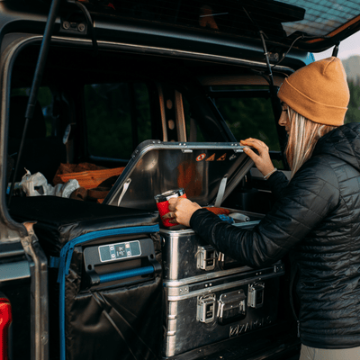 Woman in a beanie takes a mug from a stacked ZARGES K470-40810 case in the back of a vehicle