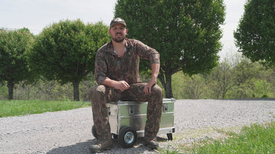 A hunter sits on a ZARGES K424 XC aluminum case with wheels and talks through why he uses it, then rolls it across gravel