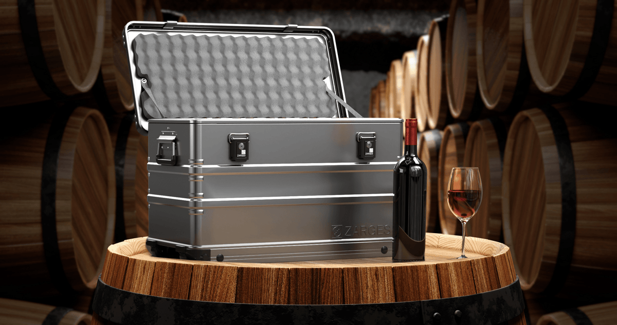 ZARGES 12 Bottle Wine Case open on an oak barrel in a cellar beside a bottle and a glass of red