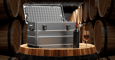 ZARGES 12 Bottle Wine Case open on an oak barrel in a cellar beside a bottle and a glass of red