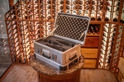 ZARGES 3 Bottle Wine Case open on a marble pedestal in a wine cellar lined with bottle racks