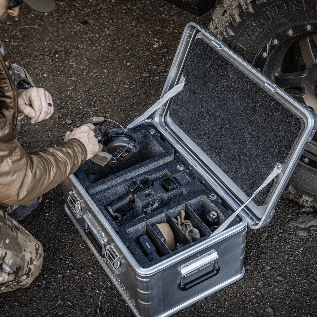 Shooter packing ear protection into a ZARGES case fitted with Chameleon foam modules beside an off-road tire