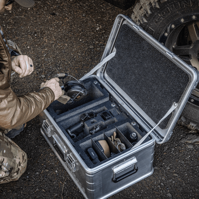 Shooter packing ear protection into a ZARGES case fitted with Chameleon foam modules beside an off-road tire