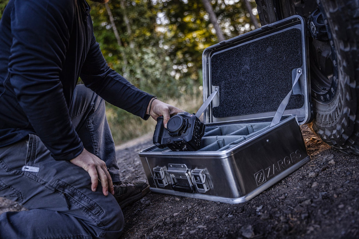 Photographer lifts a camera from an open ZARGES case on a dirt trail, gray Interior Divider Set inside