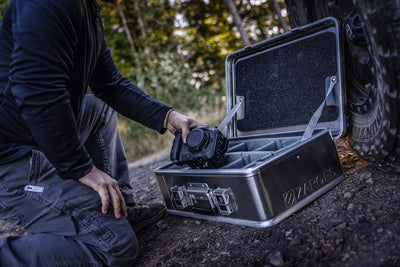 Photographer lifts a camera from an open ZARGES case on a dirt trail, gray Interior Divider Set inside