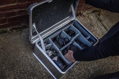 Hand placing gear into an open ZARGES case on pavement by a brick wall, Interior Divider Set compartments