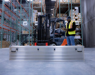 Long ZARGES K470-31004150 aluminum case on a warehouse floor, worker with a clipboard behind it