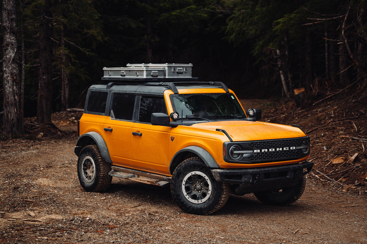 ZARGES K470-31011686 case mounted on the roof rack of an orange Bronco parked in a dark forest
