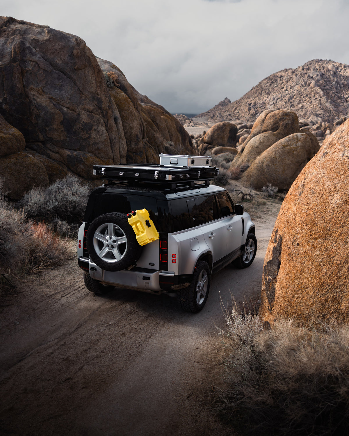 Silver SUV with ZARGES K470-380031 cases on its roof rack driving a desert trail between boulders