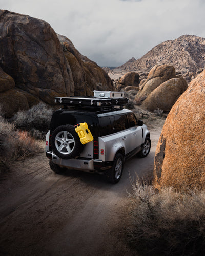 Silver SUV with ZARGES K470-380031 cases on its roof rack driving a desert trail between boulders