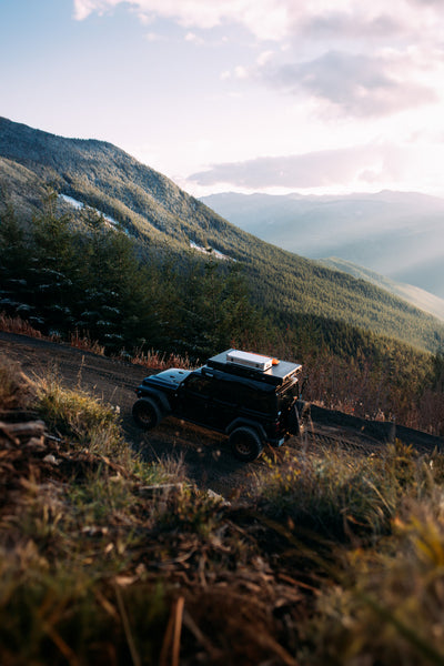 Black off-road vehicle with a ZARGES K470-380031 case on its roof rack on a mountain road at sunset