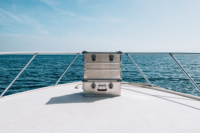 Two stacked ZARGES K470-40564 aluminum cases on the bow of a boat, open ocean ahead