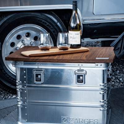ZARGES K470-40564 case used as a camp table with a wooden top, wine bottle and two glasses beside a trailer