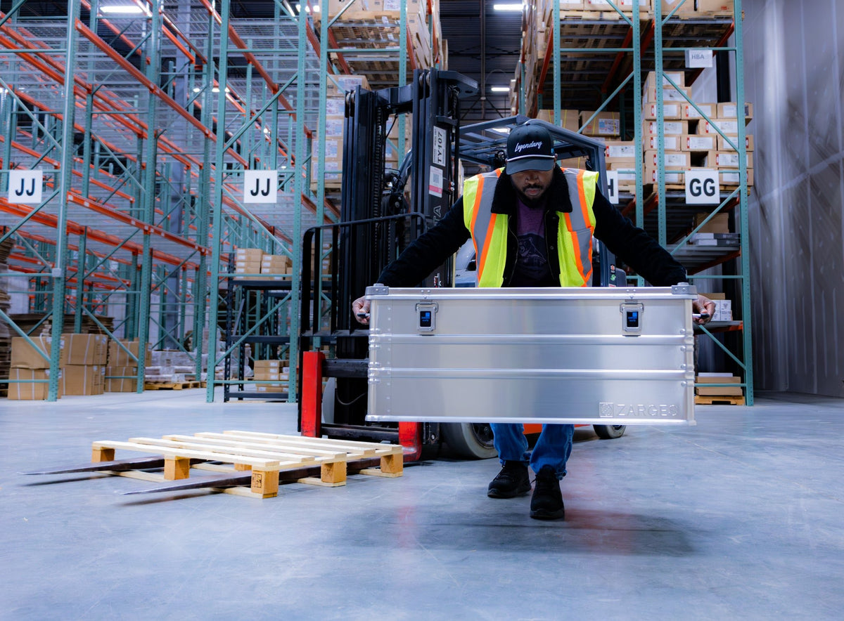 Warehouse worker in a safety vest lifting a ZARGES K470-40567 aluminum case by its side handles