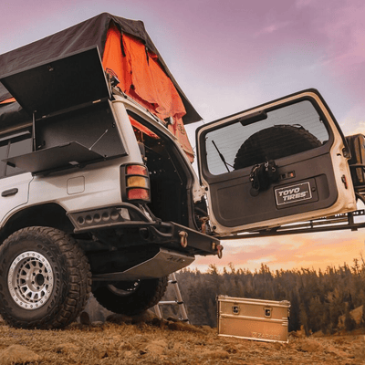 ZARGES K470-40678 case on the ground behind an overland SUV with a rooftop tent at sunset