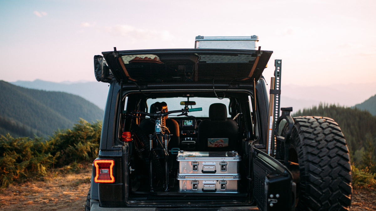 Stacked ZARGES K470-40810 cases in the open cargo area of an off-road vehicle at a mountain overlook