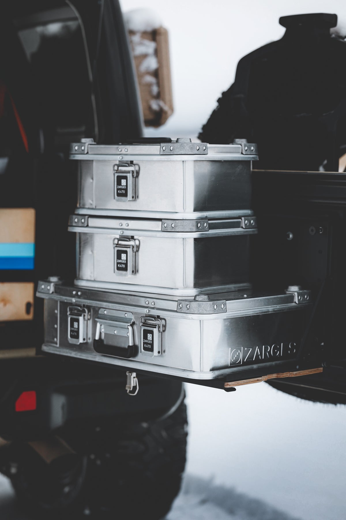 Two ZARGES K470-40835 cases stacked on a larger ZARGES case on a vehicle's rear slide-out tray in snow
