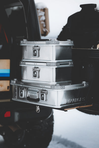 Two ZARGES K470-40835 cases stacked on a larger ZARGES case on a vehicle's rear slide-out tray in snow