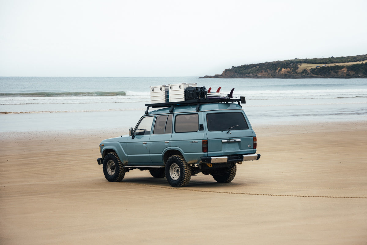 Blue SUV parked on a sandy beach carrying ZARGES K470-40839 cases on its roof rack