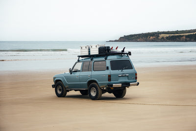 Blue SUV parked on a sandy beach carrying ZARGES K470-40839 cases on its roof rack