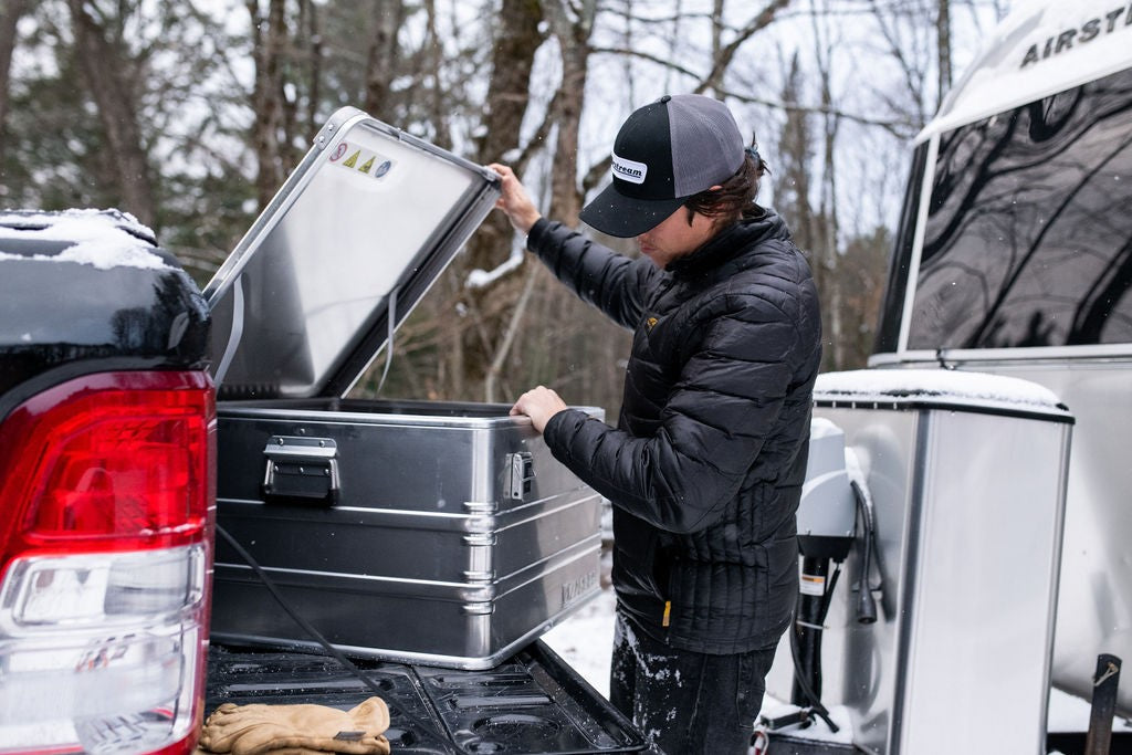 Camper lifting the lid of a ZARGES K470-40842 case in a snowy pickup bed beside a travel trailer