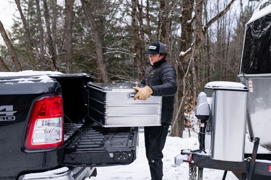 ZARGES K470-40842 aluminum case being slid into a pickup truck bed at a snowy forest campsite