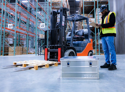 ZARGES K470-40842 aluminum case on a warehouse floor beside a forklift as a worker reviews a clipboard