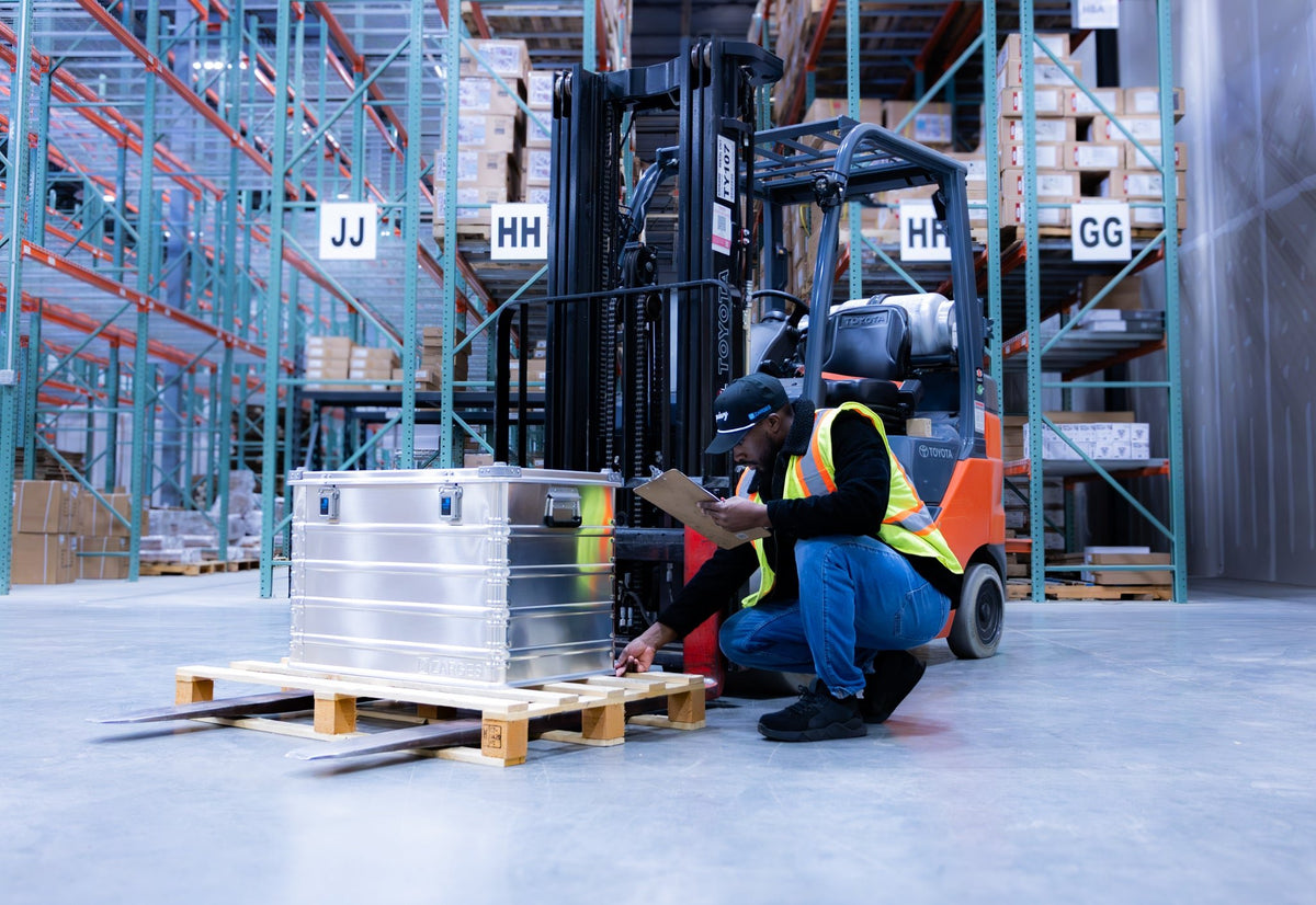 Worker kneeling to inspect a ZARGES K470-40844 case on a pallet in a warehouse