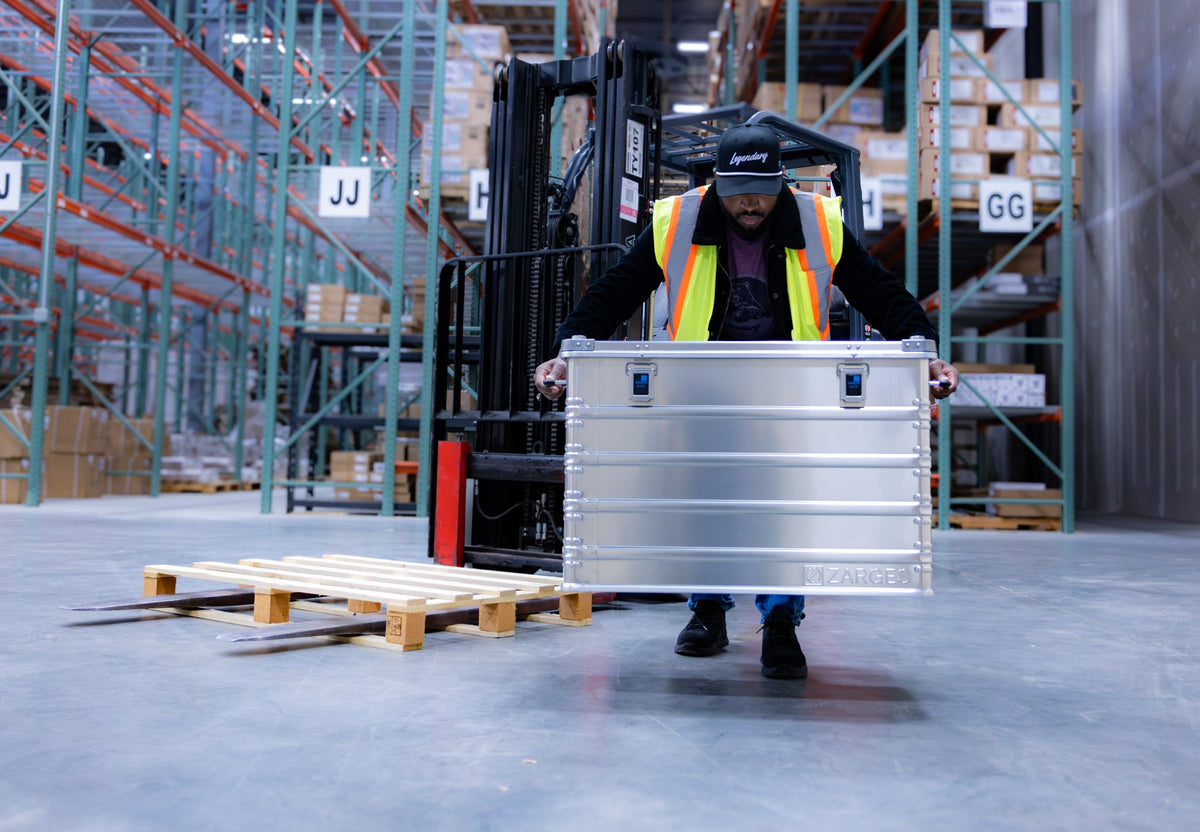 Warehouse worker in a safety vest carrying a ZARGES K470-40844 case past a forklift
