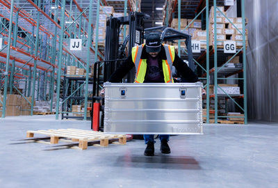 Warehouse worker in a safety vest carries a ZARGES K470-40846 case by its end handles