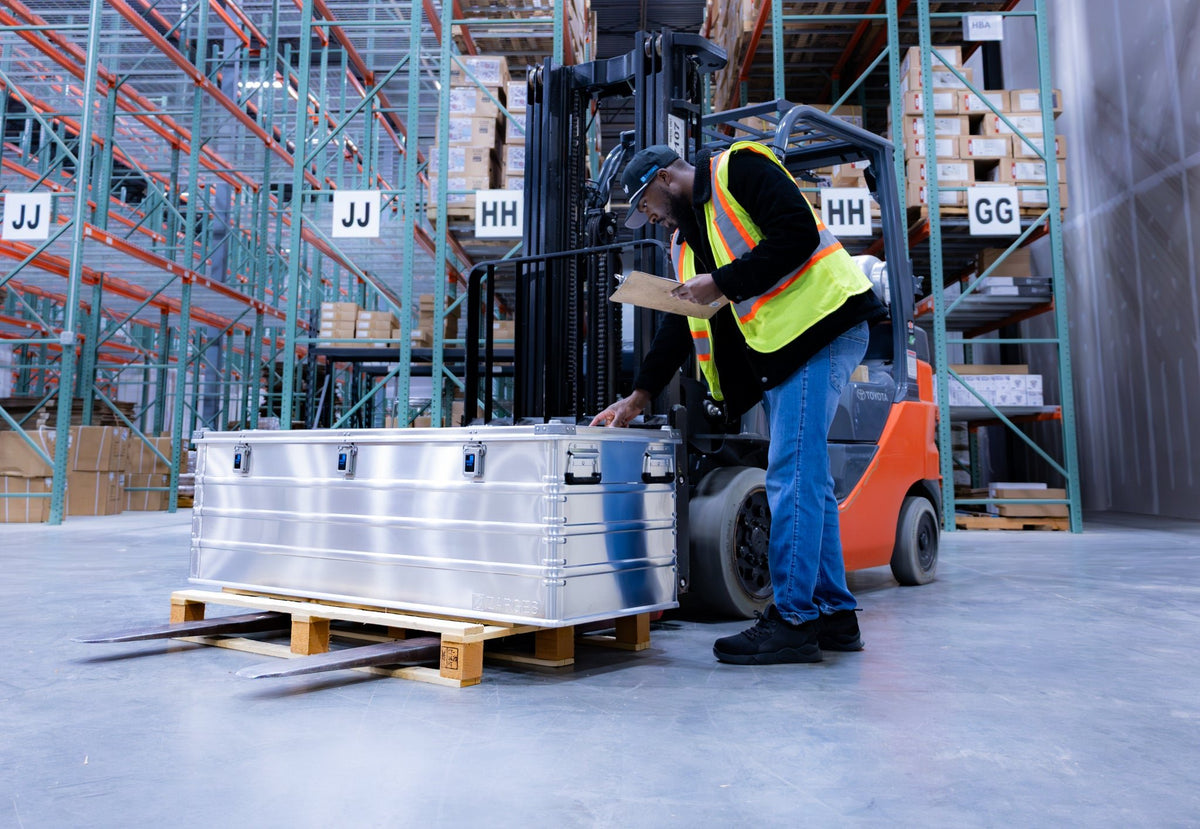 Warehouse worker inspects a ZARGES K470-40875 long case set on a wooden pallet near a forklift