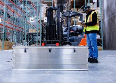 ZARGES K470-40875 long case on a warehouse floor as a worker in a safety vest checks a clipboard by a forklift