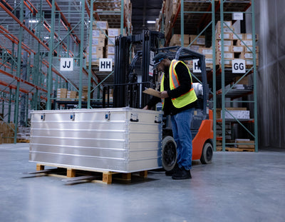 Warehouse worker with a clipboard beside a ZARGES K470-40876 large aluminum case on a pallet
